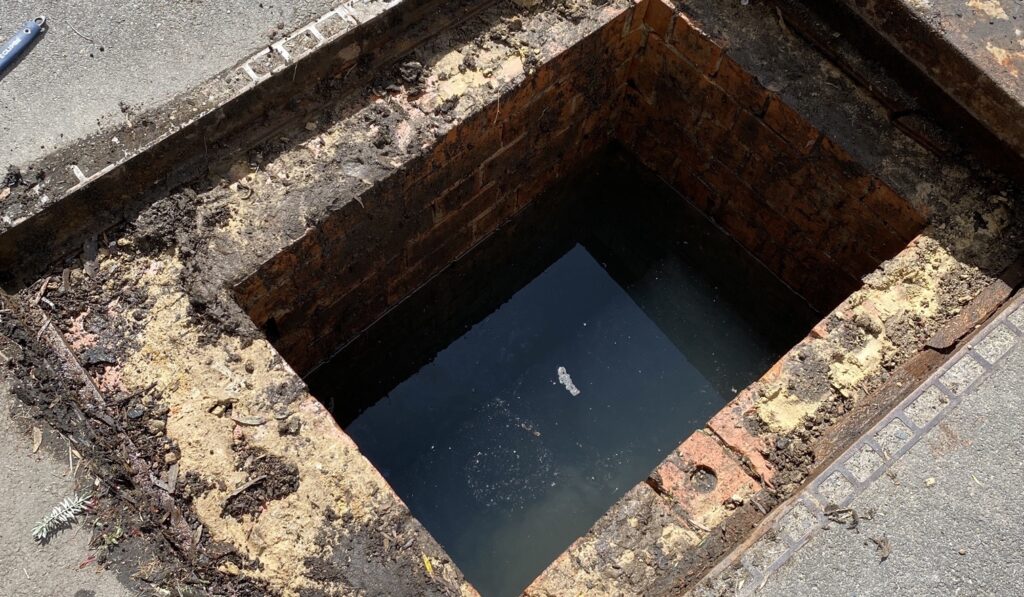 Open brick stormwater pit at the kerb, filled with standing water