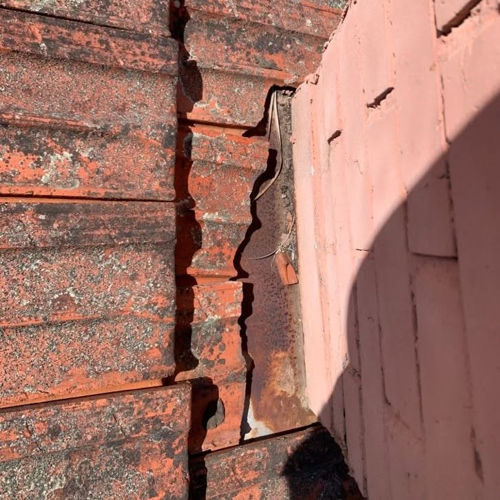 Gap and rusted old flashing between roof tiles and a rendered chimney in Glen Iris.